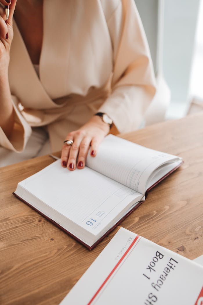 Adult woman writing in an open notebook at a wooden desk, focusing on reading and note-taking.